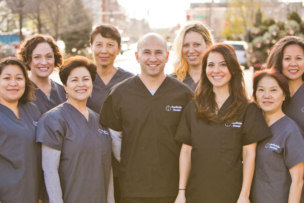 Group of Dentists and Dental assistants standing together outside on a warmly-lit sunny afternoon wearing dark grey and dark blue medical outfits